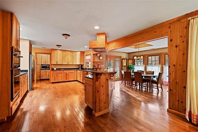 kitchen with a breakfast bar, hanging light fixtures, light hardwood / wood-style floors, kitchen peninsula, and stainless steel appliances