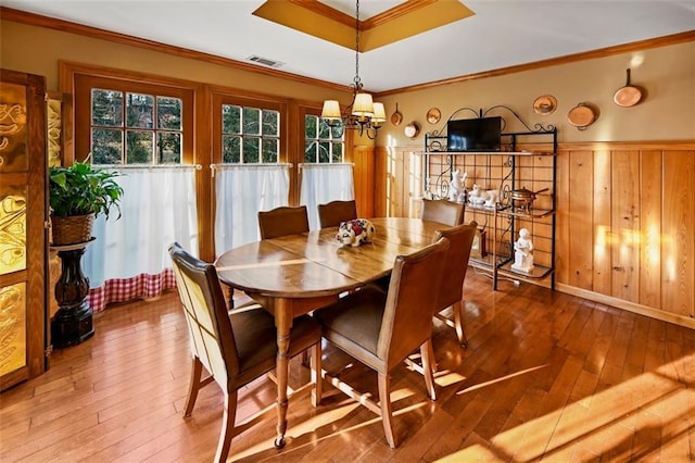 dining space featuring an inviting chandelier, wood-type flooring, ornamental molding, and wood walls