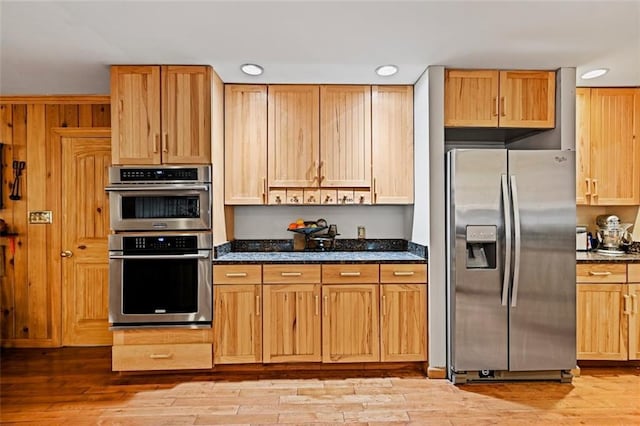 kitchen featuring stainless steel appliances, light hardwood / wood-style floors, and dark stone counters