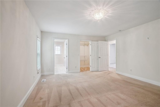 unfurnished bedroom with visible vents, baseboards, a spacious closet, ensuite bathroom, and carpet flooring