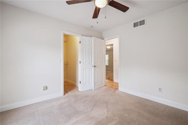 unfurnished bedroom with a walk in closet, carpet, a ceiling fan, baseboards, and visible vents