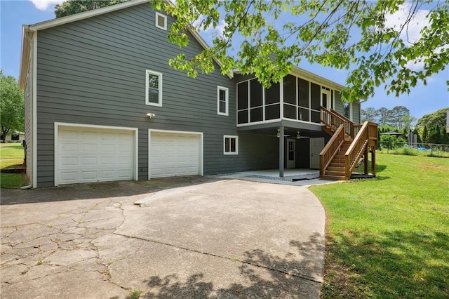 rear view of house with a garage, a sunroom, stairway, concrete driveway, and a lawn