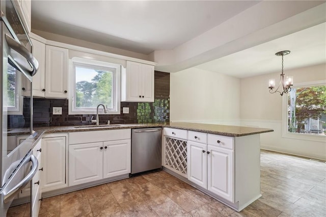 kitchen with a peninsula, tasteful backsplash, a sink, dishwasher, and a notable chandelier