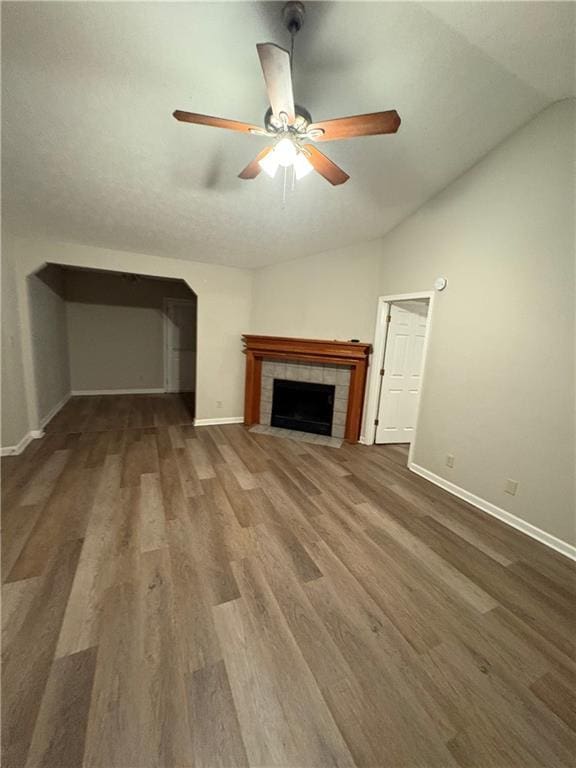 unfurnished living room featuring ceiling fan, dark hardwood / wood-style flooring, a tile fireplace, and vaulted ceiling