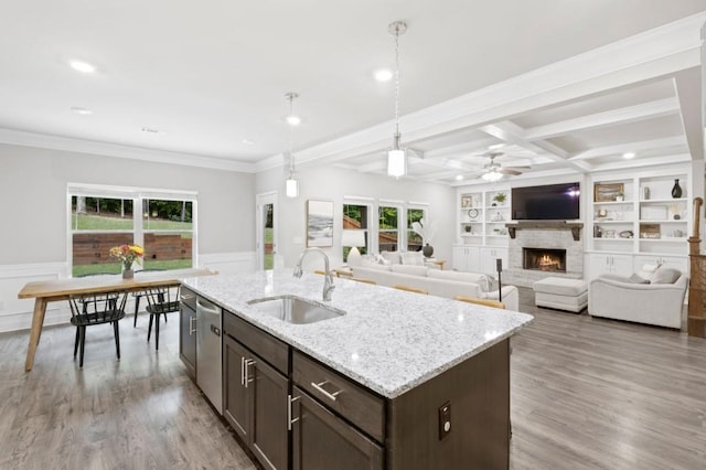 kitchen featuring a kitchen island with sink, light wood-type flooring, sink, light stone countertops, and stainless steel dishwasher