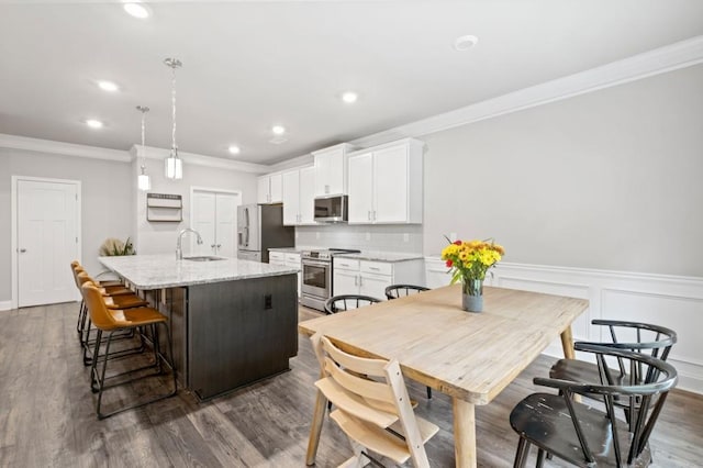 kitchen with white cabinets, a kitchen island with sink, decorative light fixtures, dark wood-type flooring, and stainless steel appliances