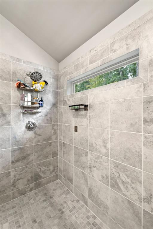 bathroom with tiled shower and vaulted ceiling