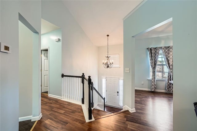 hallway featuring a notable chandelier, dark wood-type flooring, an upstairs landing, and baseboards