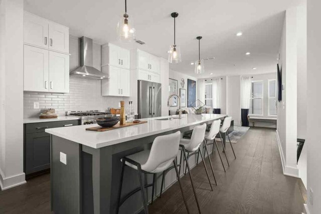 kitchen with dark hardwood / wood-style floors, high quality fridge, a center island with sink, and wall chimney range hood