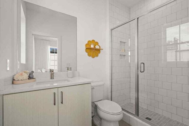 bathroom featuring a shower with shower door, toilet, and vanity