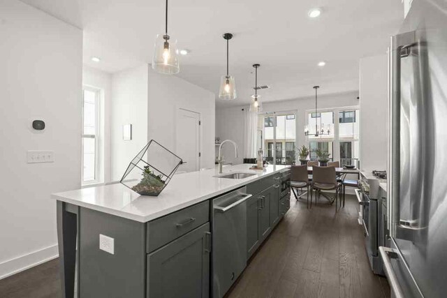 kitchen with sink, a kitchen island with sink, pendant lighting, high end appliances, and dark wood-type flooring