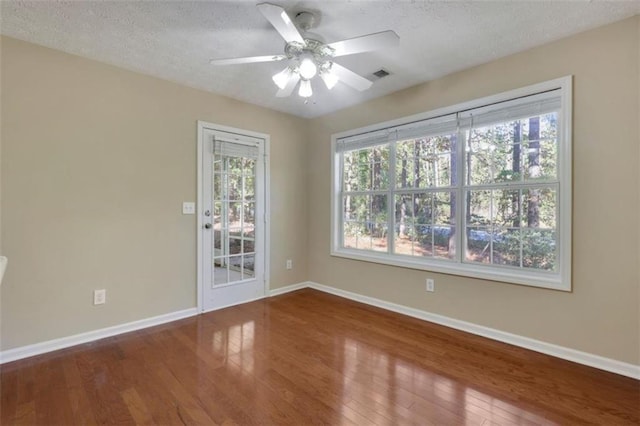 empty room with hardwood / wood-style floors, a wealth of natural light, ceiling fan, and a textured ceiling