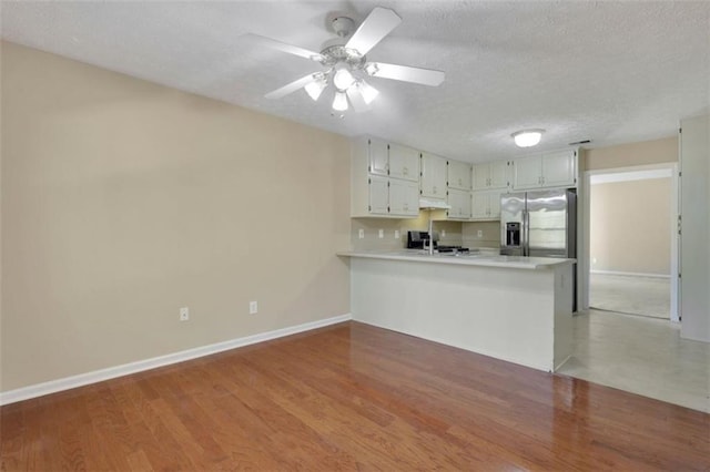 kitchen with white cabinets, light hardwood / wood-style flooring, stainless steel fridge with ice dispenser, and kitchen peninsula