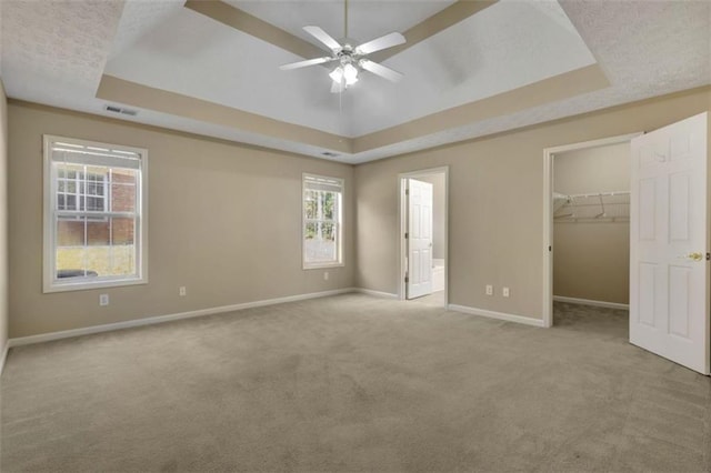 unfurnished bedroom featuring a closet, a tray ceiling, a spacious closet, and light colored carpet