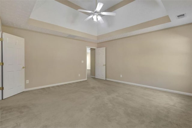 carpeted spare room featuring a tray ceiling and ceiling fan