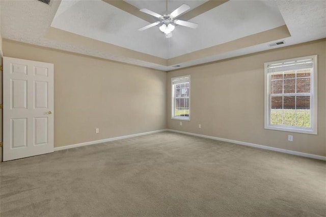 empty room with a raised ceiling, ceiling fan, and carpet floors