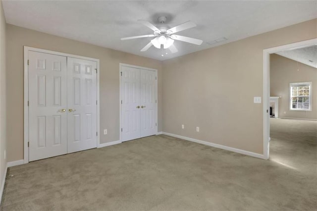 unfurnished bedroom with light colored carpet, two closets, and ceiling fan