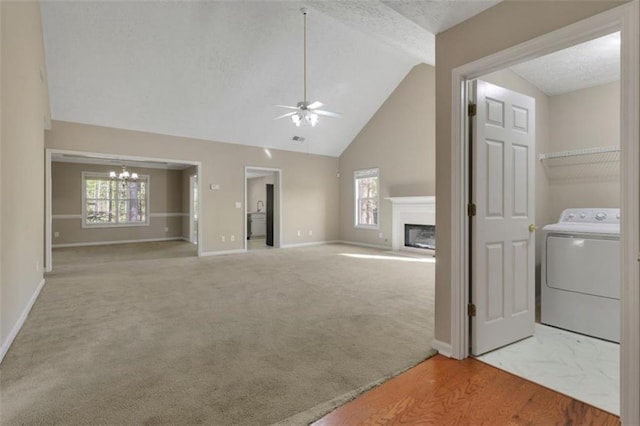 unfurnished living room with ceiling fan with notable chandelier, high vaulted ceiling, carpet floors, and washer / dryer