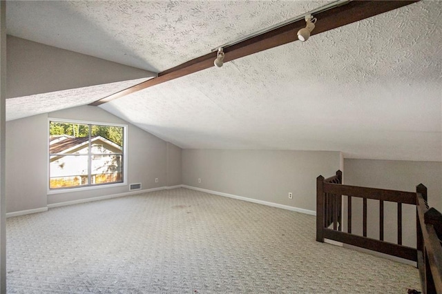 additional living space with a textured ceiling, visible vents, carpet floors, baseboards, and lofted ceiling