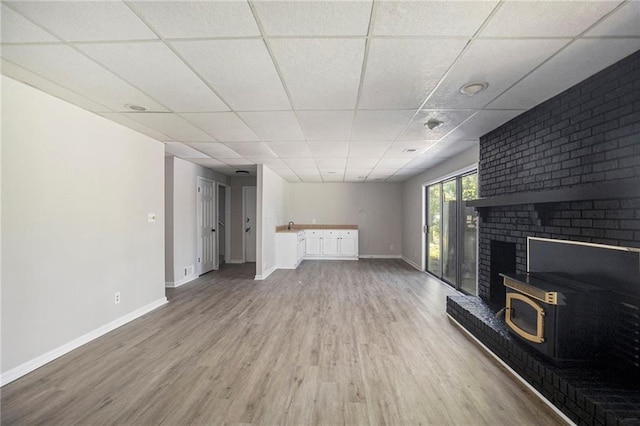 unfurnished living room with wood finished floors, a fireplace, baseboards, a paneled ceiling, and a sink
