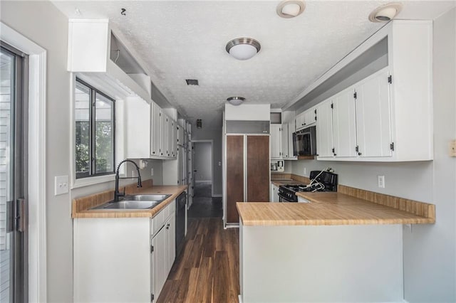 kitchen with dark wood-style flooring, gas range oven, a textured ceiling, white cabinetry, and a sink