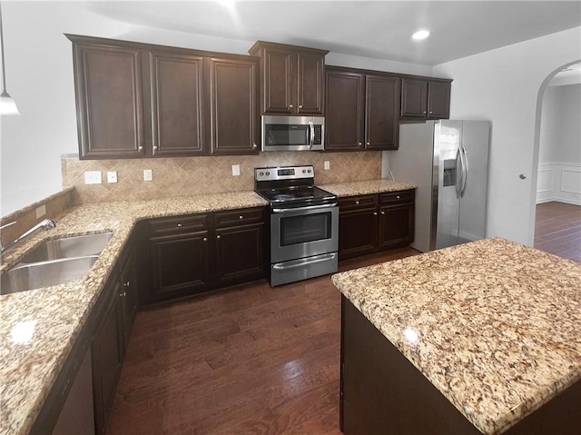 kitchen with arched walkways, dark wood-type flooring, stainless steel appliances, dark brown cabinets, and a sink