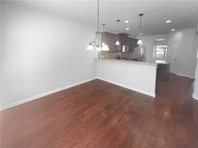 kitchen featuring arched walkways, appliances with stainless steel finishes, dark wood-type flooring, a peninsula, and baseboards