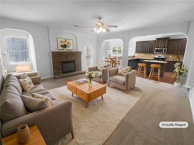 living room with arched walkways, ceiling fan, a stone fireplace, and a wealth of natural light