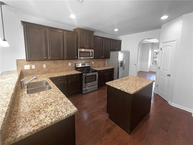 kitchen with arched walkways, dark brown cabinetry, a sink, appliances with stainless steel finishes, and dark wood-style floors