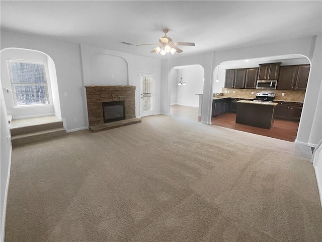 unfurnished living room with arched walkways, baseboards, ceiling fan, carpet, and a fireplace