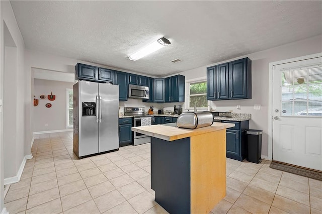 1328 Hidden Hills Pkwy, Stone Mountain, GA 30088 - kitchen with appliances with stainless steel finishes, blue cabinets, a textured ceiling, light tile patterned floors, and butcher block countertops