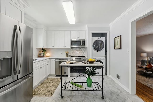 kitchen featuring appliances with stainless steel finishes, stacked washer and dryer, white cabinets, and light countertops