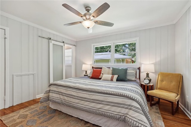 bedroom with ornamental molding, ceiling fan, a barn door, and wood finished floors