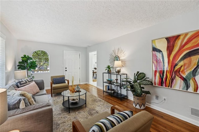 living room featuring visible vents, a textured ceiling, baseboards, and wood finished floors