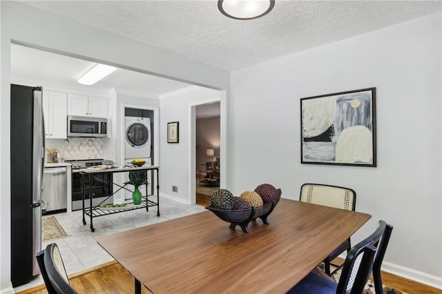 dining space with a textured ceiling, stacked washer and dryer, and baseboards