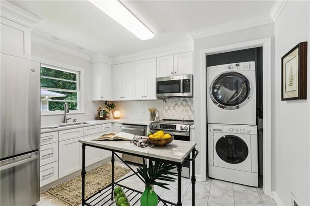 kitchen with appliances with stainless steel finishes, stacked washing maching and dryer, and white cabinetry