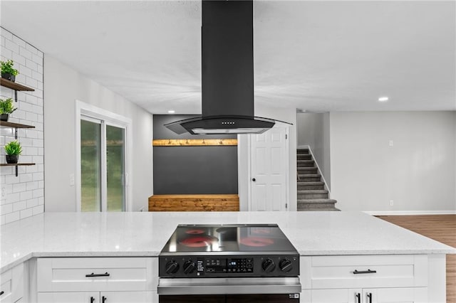 kitchen featuring stainless steel range, island range hood, decorative backsplash, and white cabinets