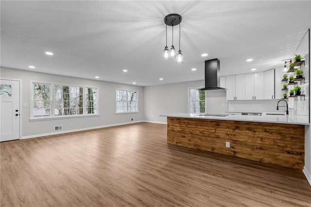 kitchen featuring white cabinets, hanging light fixtures, island exhaust hood, hardwood / wood-style flooring, and kitchen peninsula