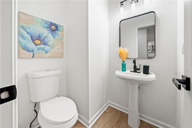 half bathroom with baseboards, toilet, and wood finished floors