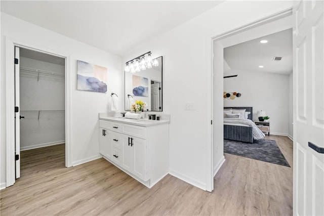 bathroom featuring wood finished floors, visible vents, baseboards, double vanity, and recessed lighting