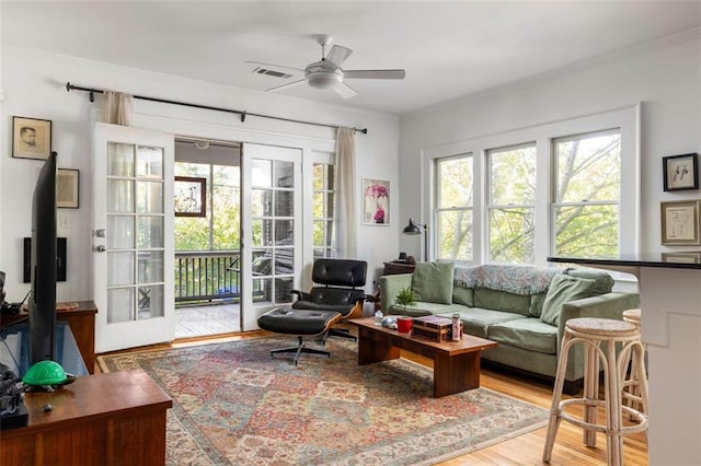 living area with light wood-style floors, visible vents, crown molding, and ceiling fan