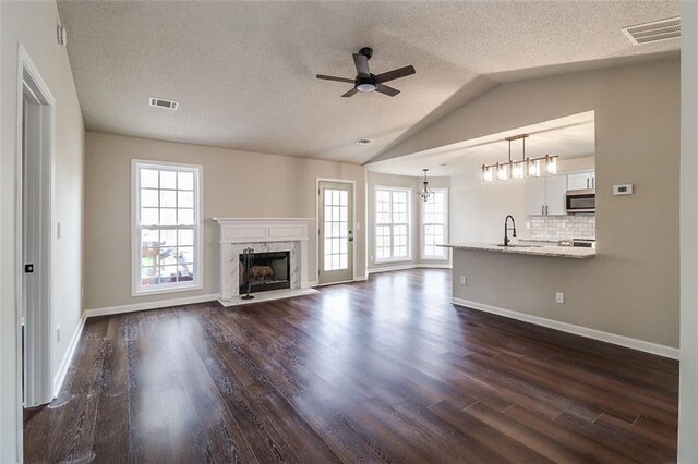 unfurnished living room featuring a high end fireplace, a textured ceiling, dark hardwood / wood-style floors, and vaulted ceiling