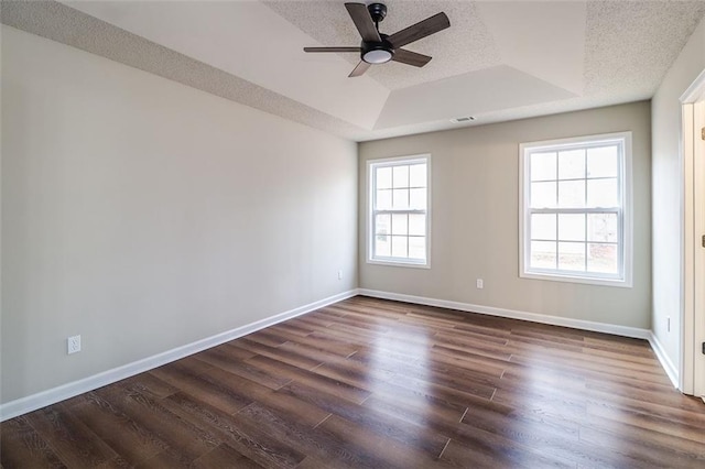 spare room with a textured ceiling, a tray ceiling, a wealth of natural light, and dark wood-type flooring