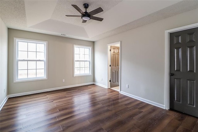 unfurnished bedroom with dark hardwood / wood-style floors, ceiling fan, a textured ceiling, and a tray ceiling