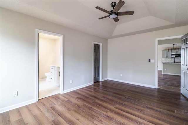 unfurnished bedroom with connected bathroom, ceiling fan, dark wood-type flooring, a raised ceiling, and vaulted ceiling