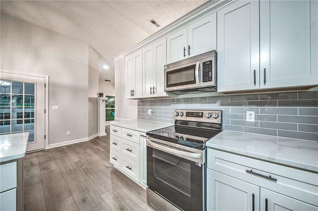 220 Chandler Ct, Sugar Hill, GA 30518 - kitchen featuring stainless steel appliances, vaulted ceiling, wood finished floors, tasteful backsplash, and light stone counters