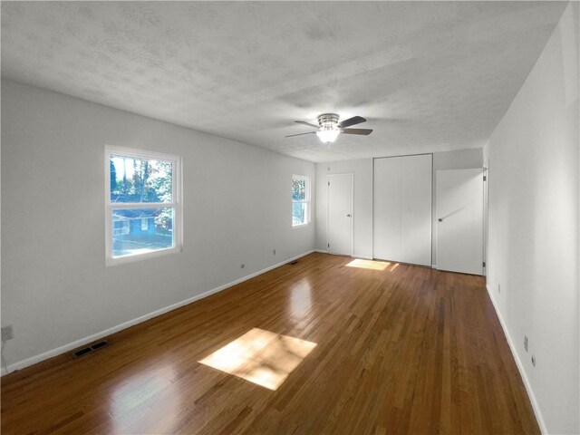 unfurnished bedroom with ceiling fan, wood-type flooring, a textured ceiling, and multiple windows