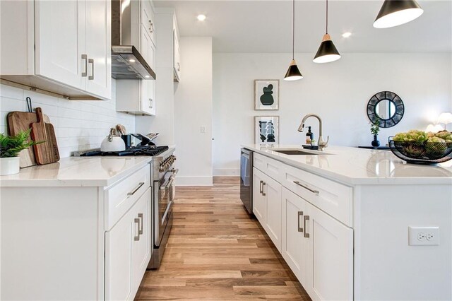 kitchen featuring appliances with stainless steel finishes, wall chimney range hood, pendant lighting, light stone counters, and sink