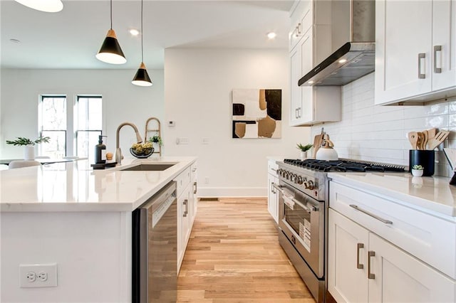 kitchen with pendant lighting, white cabinets, wall chimney range hood, stainless steel appliances, and a center island with sink