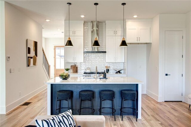 kitchen featuring pendant lighting, white cabinets, a center island with sink, and backsplash